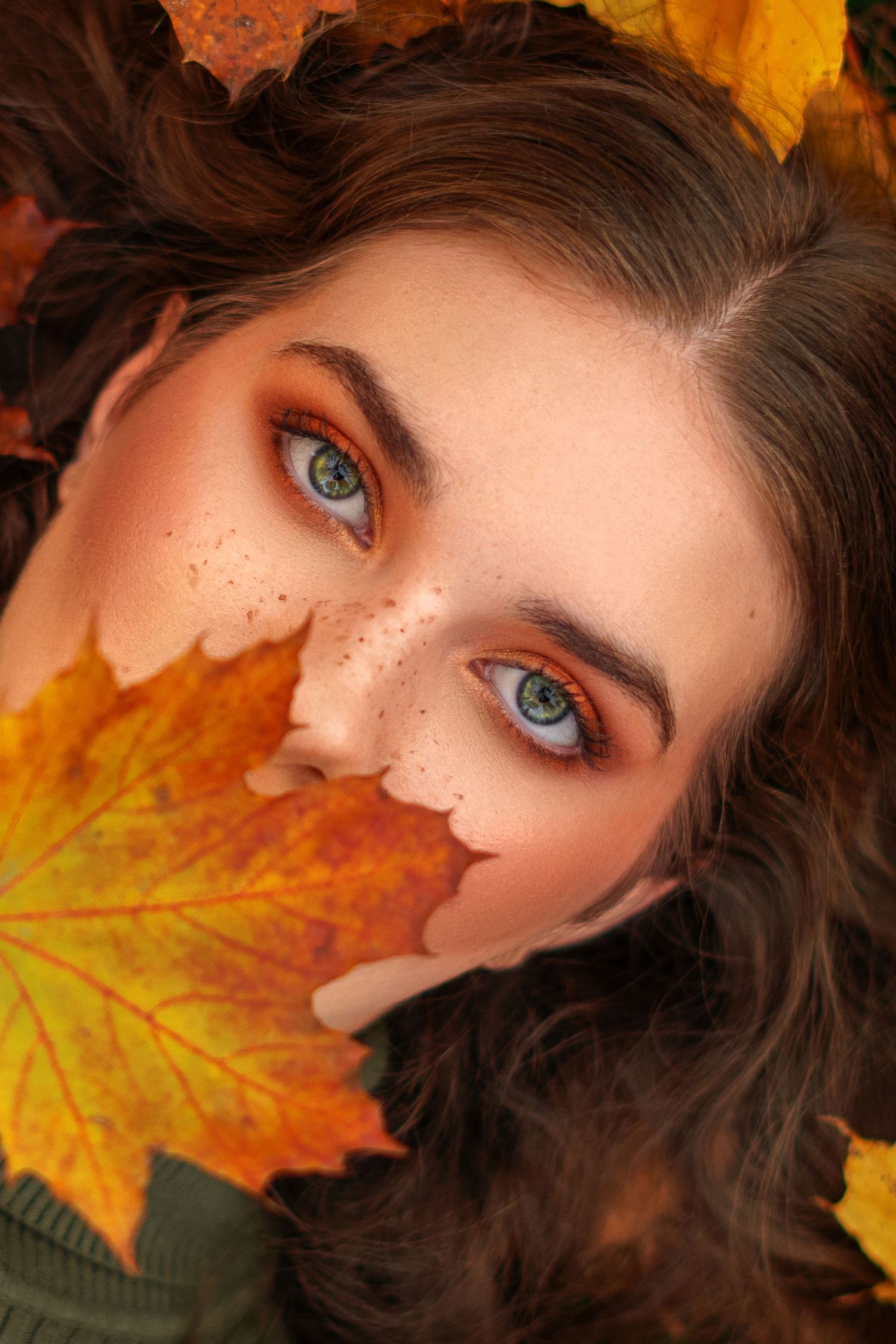 Autumn-themed beauty shot with orange eyeshadow and maple leaf covering half the face.