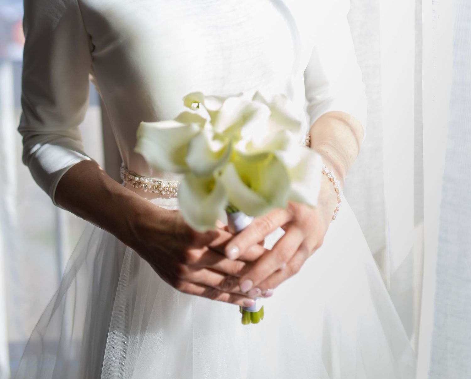 A delicate bouquet of white calla lilies is held gently against a white wedding dress.