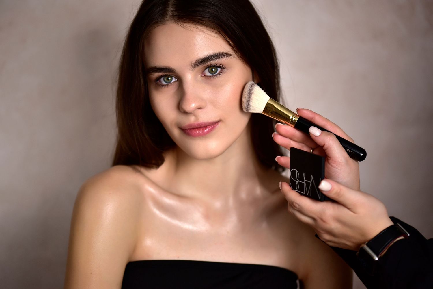 Makeup application in progress with a professional brush against neutral background.