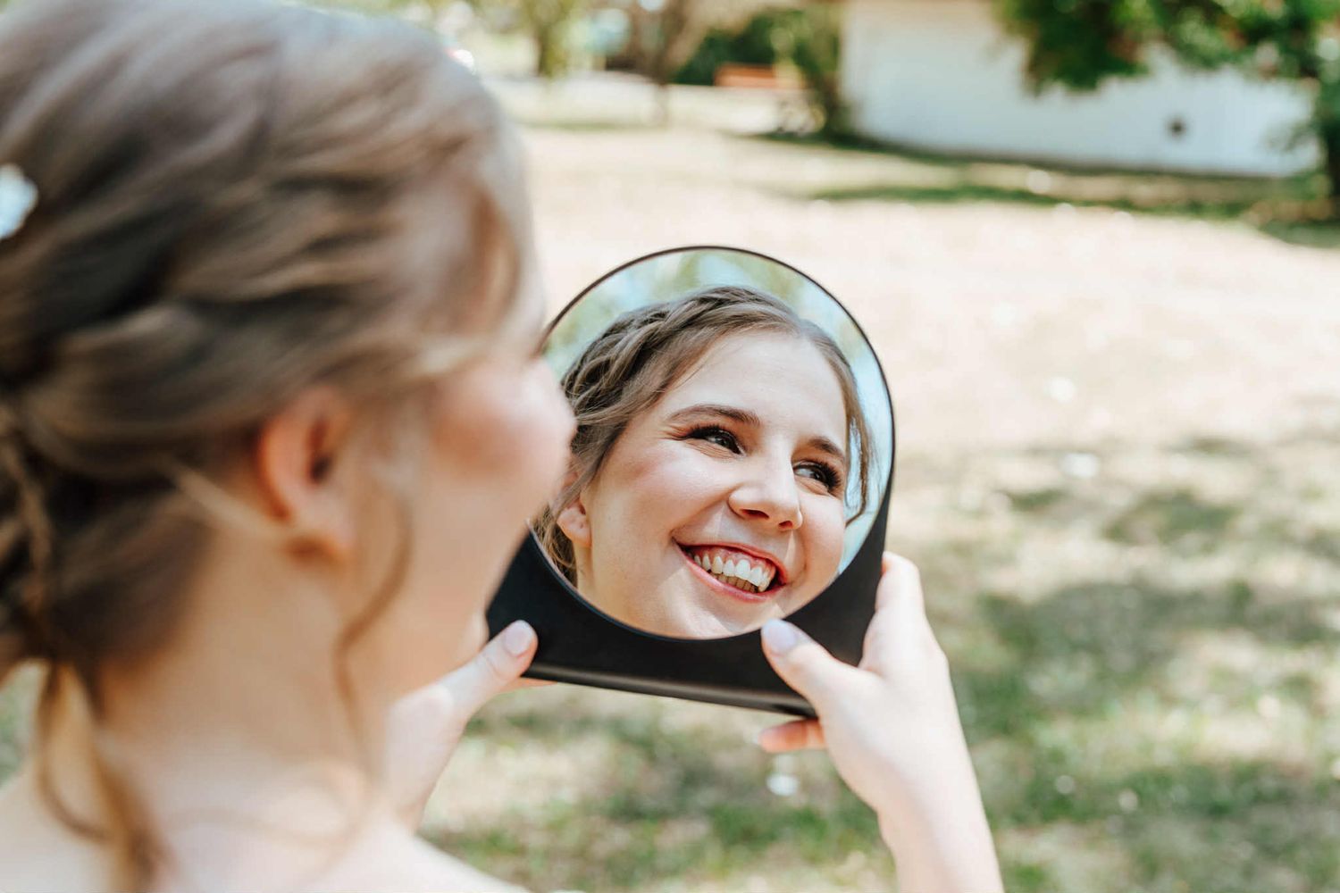 Person holding mirror in outdoor setting with trees and natural lighting making multiple reflections.