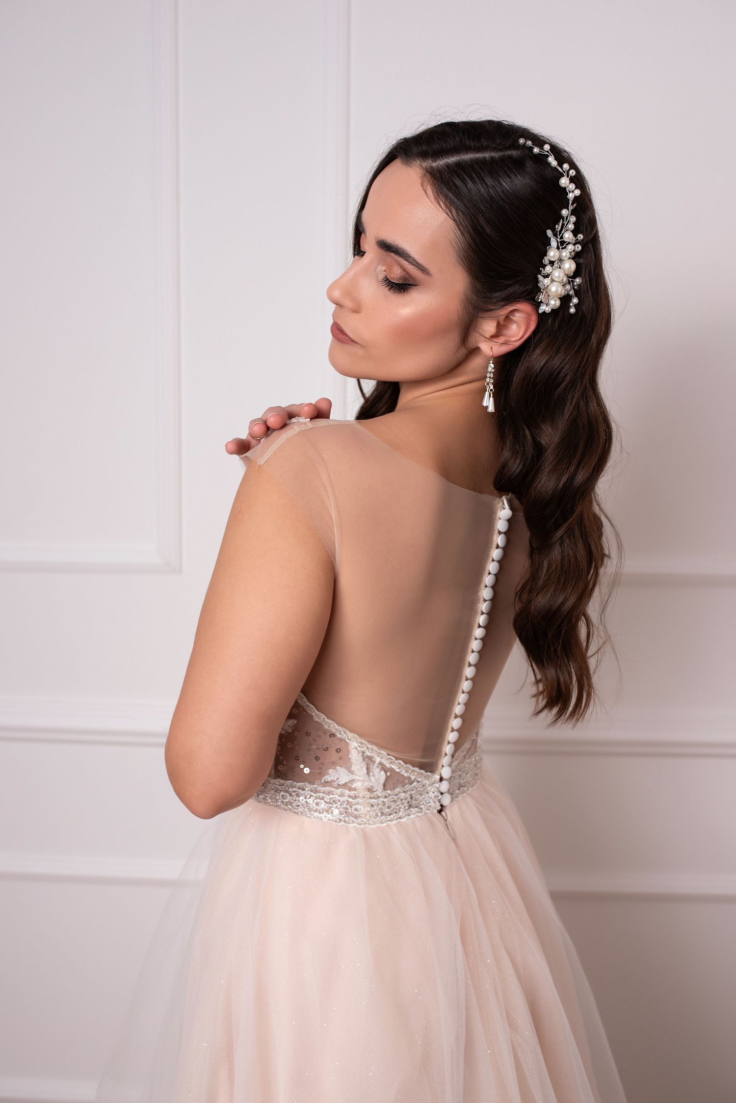 Close-up of elegant bridal hairstyle with pearl accessories and sheer back wedding dress in ivory.