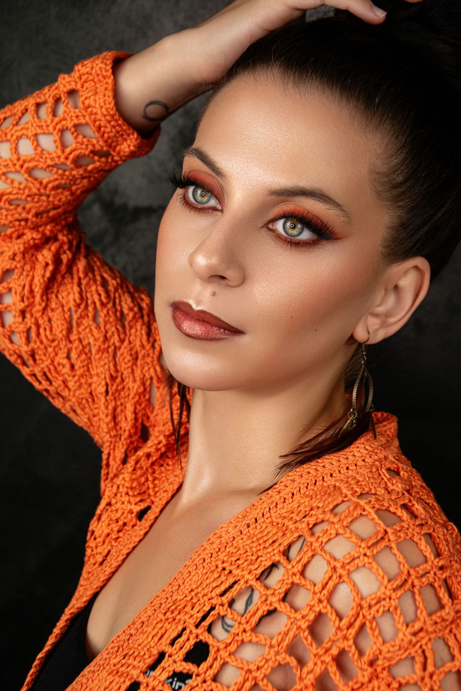 Fashion portrait in vibrant orange crochet top with dramatic makeup and striking pose.