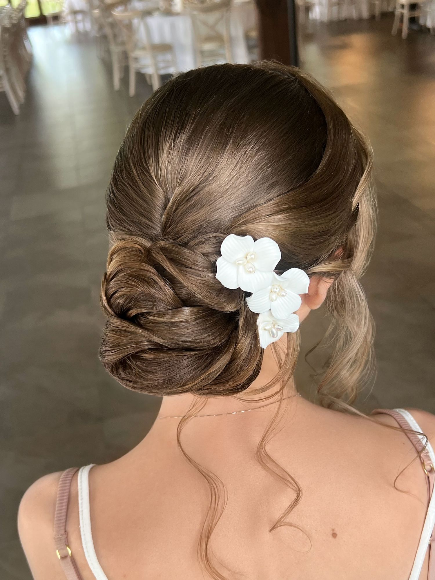 Elegant bridal updo with twisted low bun and white floral hair accessories, perfect for weddings.