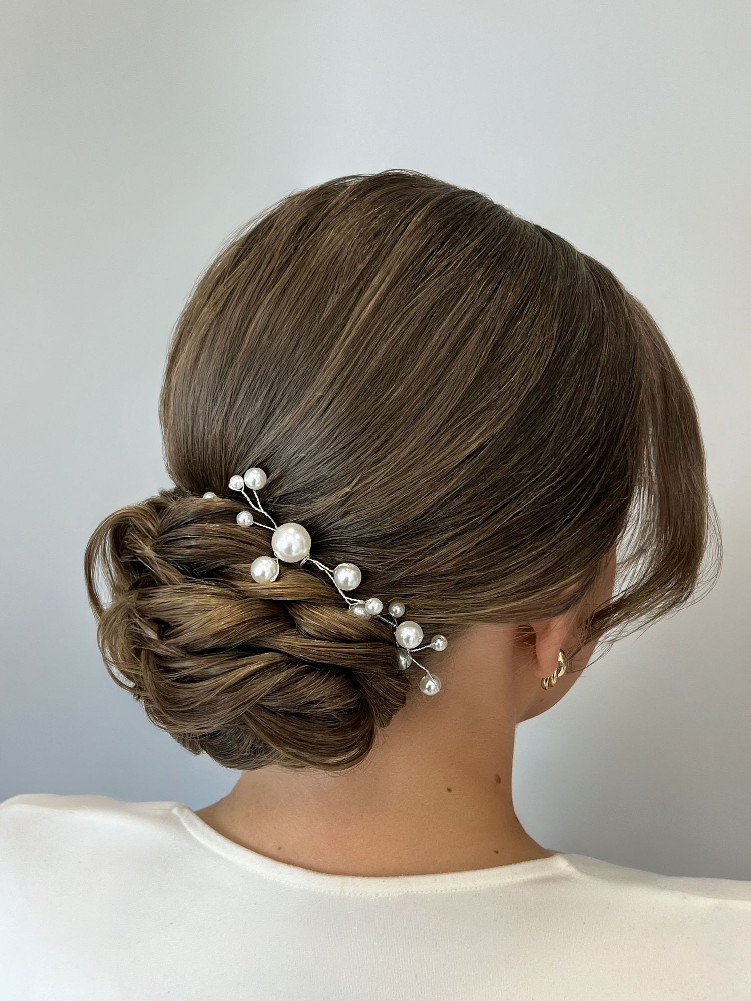 Elegant bridal updo with pearl hair pins, featuring a low chignon on brunette hair.
