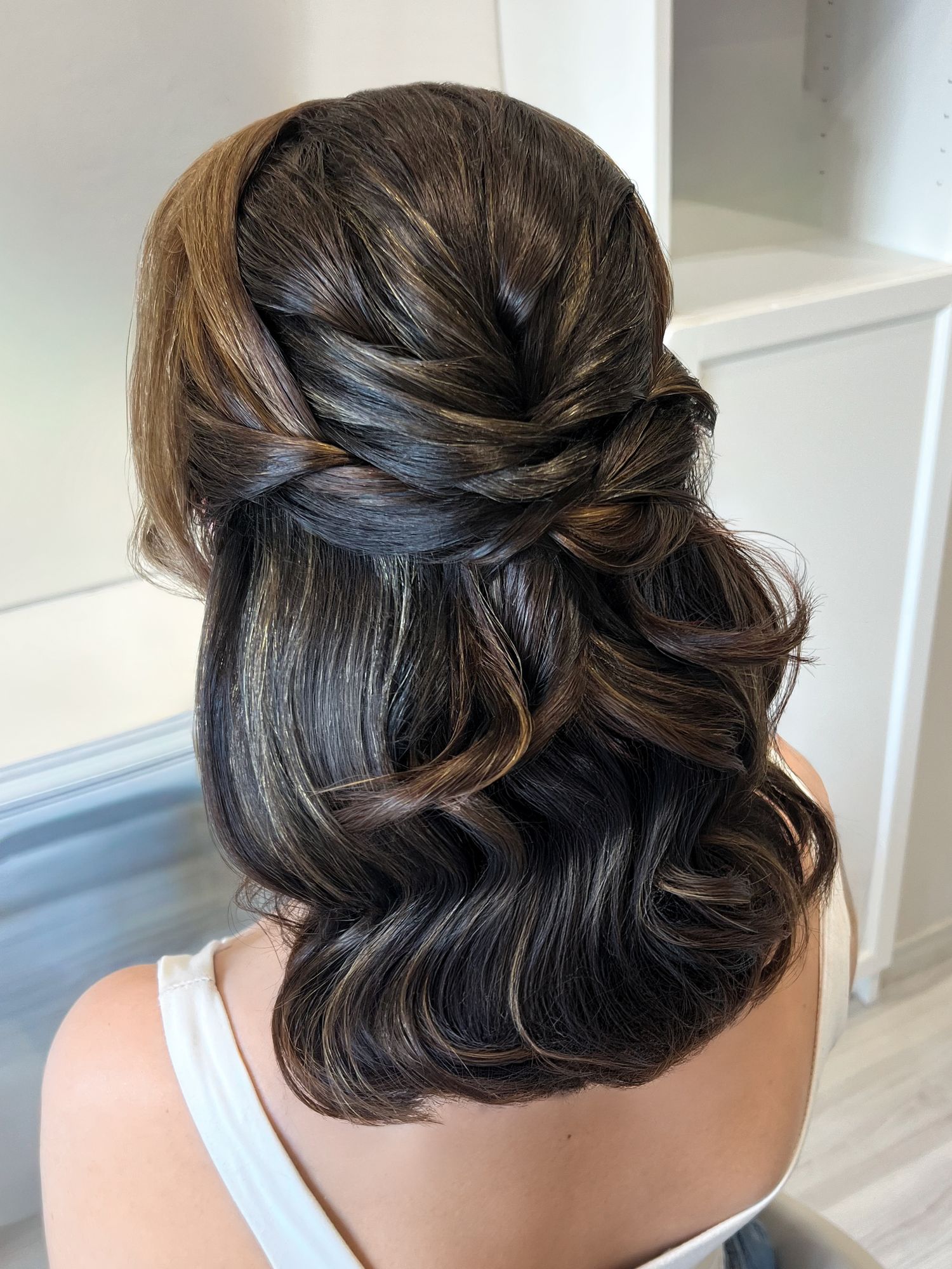 Elegant half-up half-down hairstyle with soft curls and twisted detail, perfect for weddings or formal events.