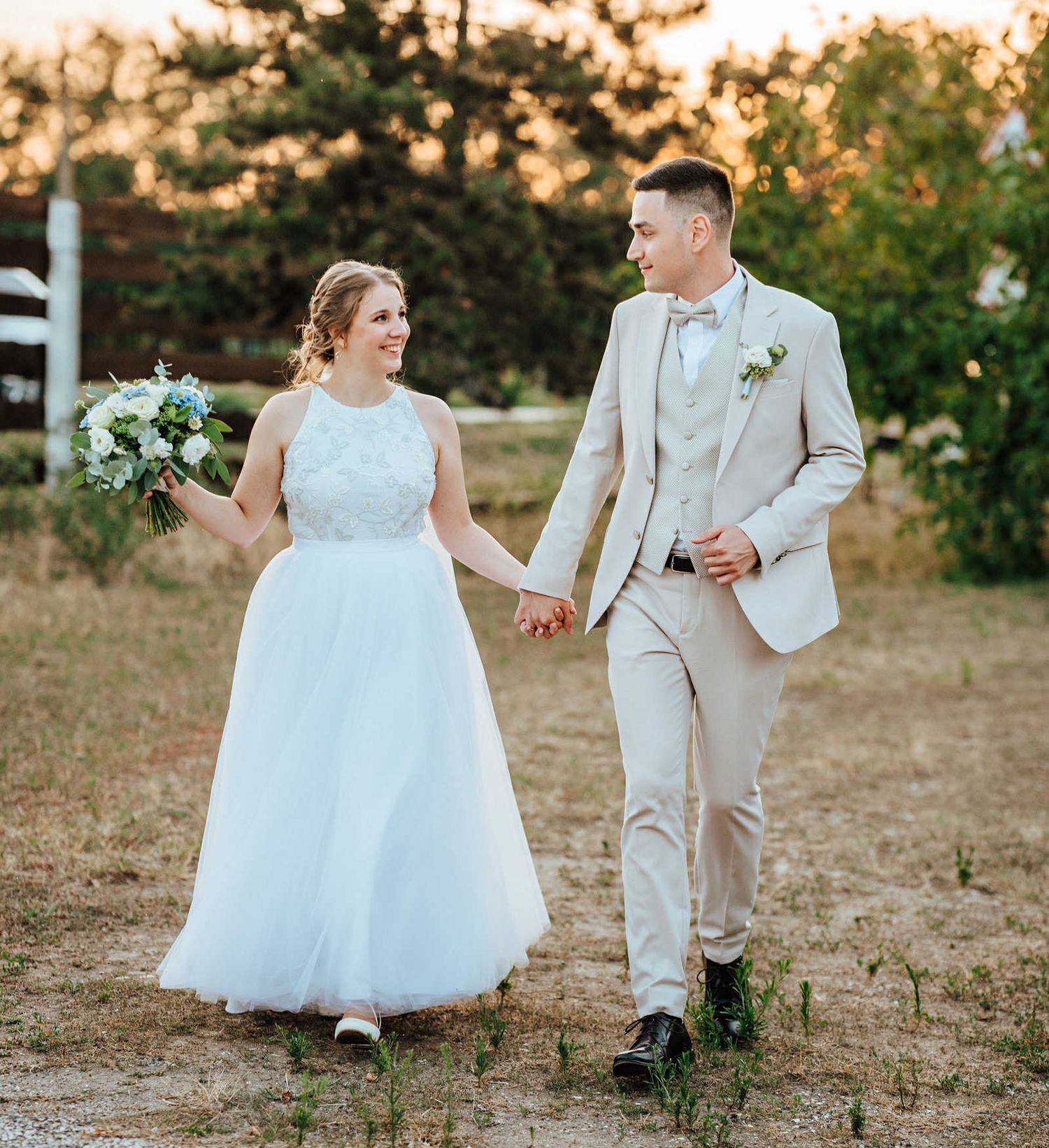 A couple and flower girl share a light-hearted moment walking together outdoors during golden hour.