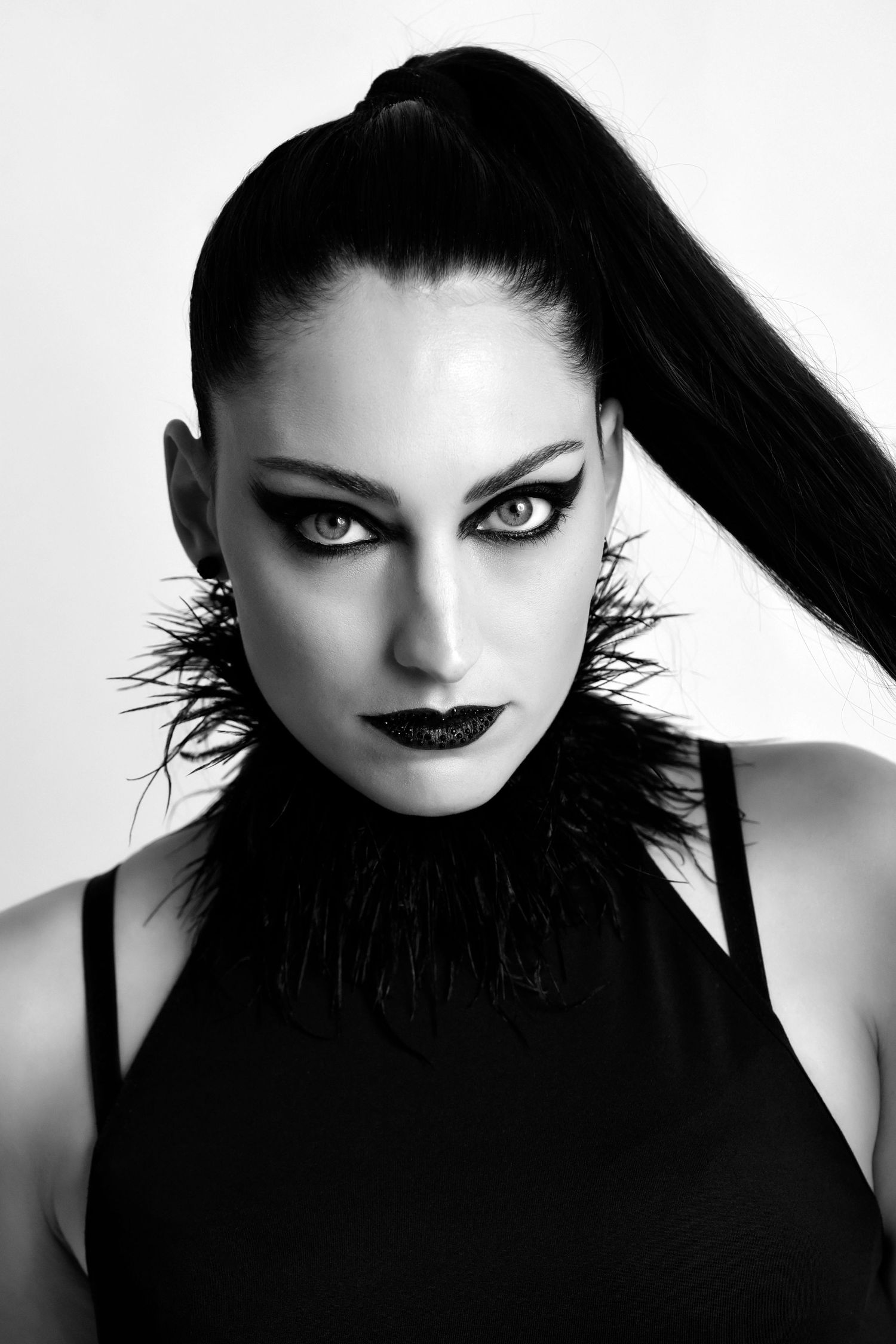 High contrast black and white portrait with dramatic makeup and feather collar detail.