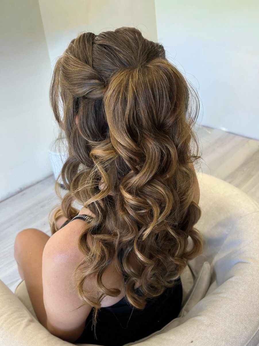 Half-up half-down hairstyle with braided crown and loose curls, featuring warm brunette balayage highlights.