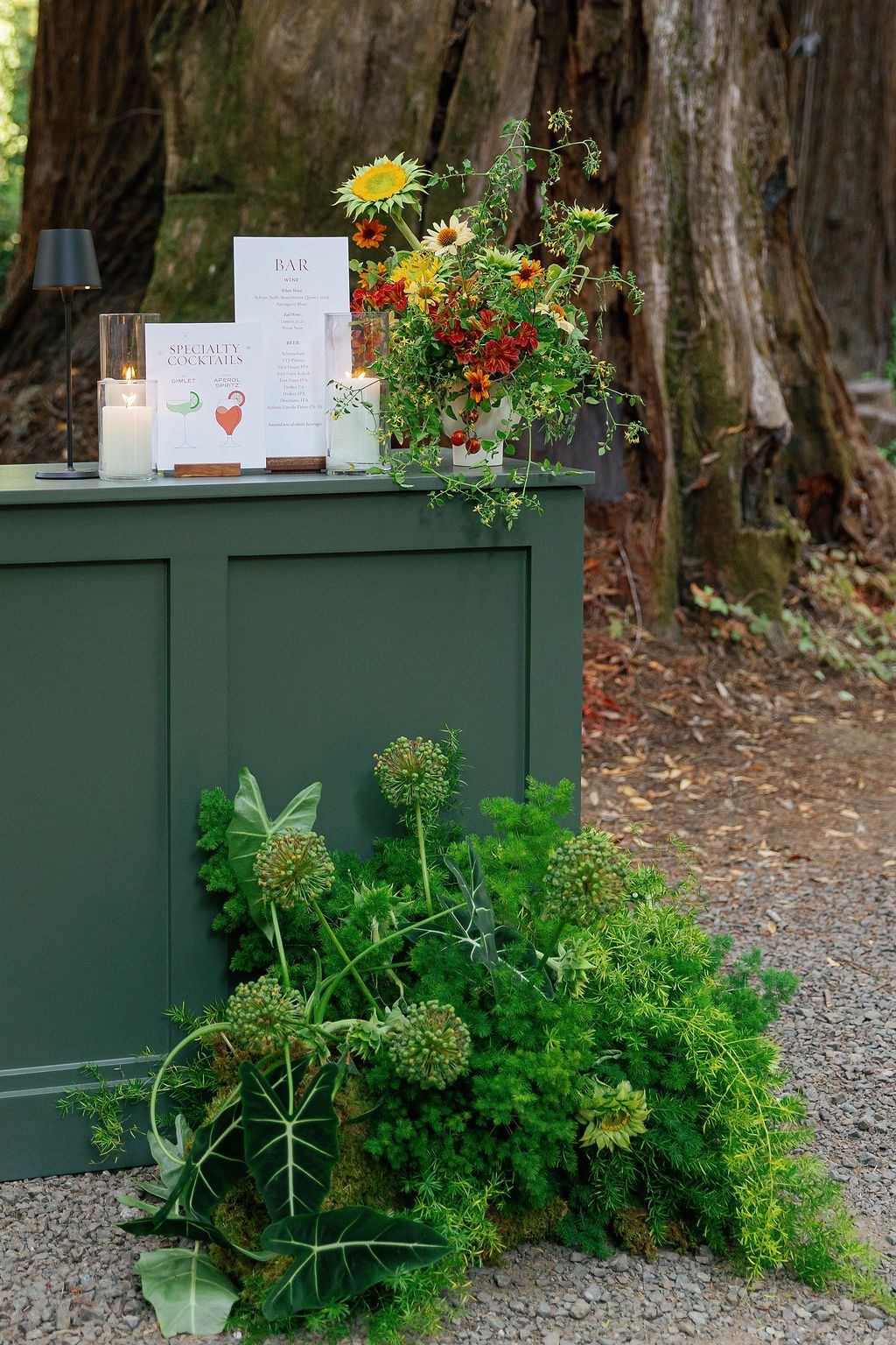 Green wooden cabinet decorated with vibrant floral arrangements and signage in a forest setting.