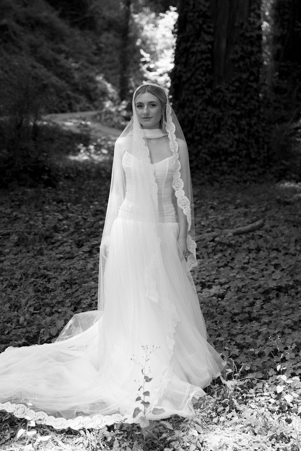 Black and white bridal portraits showing flowing white wedding dress and veil against a dark forest background.