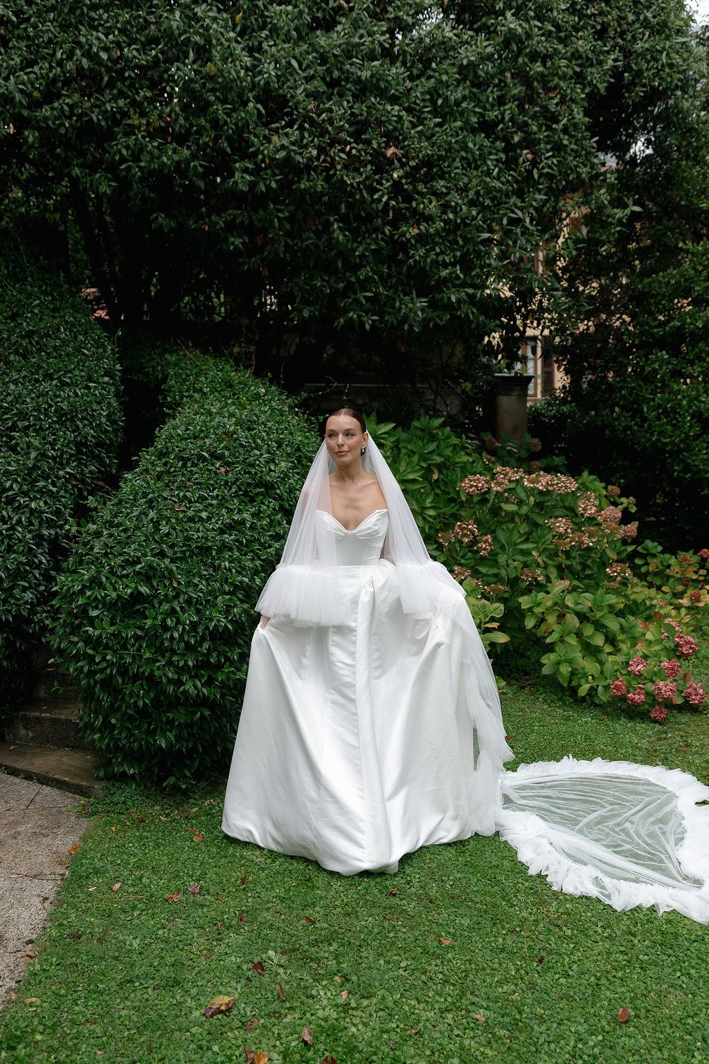 A flowing white wedding dress photographed in a lush garden setting with green foliage in Lake Como.