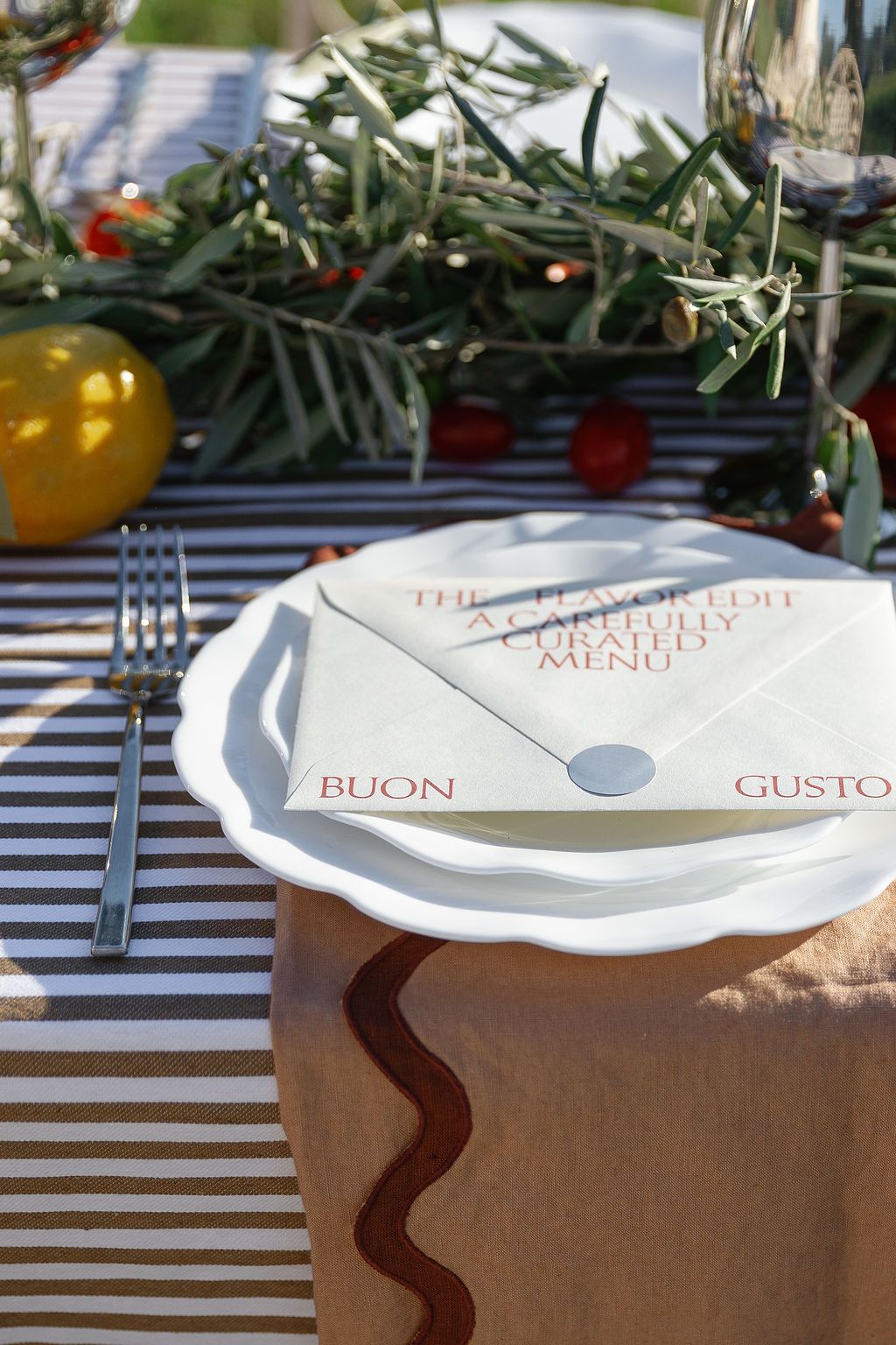 White ceramic plates with 'Buon Gusto' text arranged on a rustic wooden surface with olive branches.