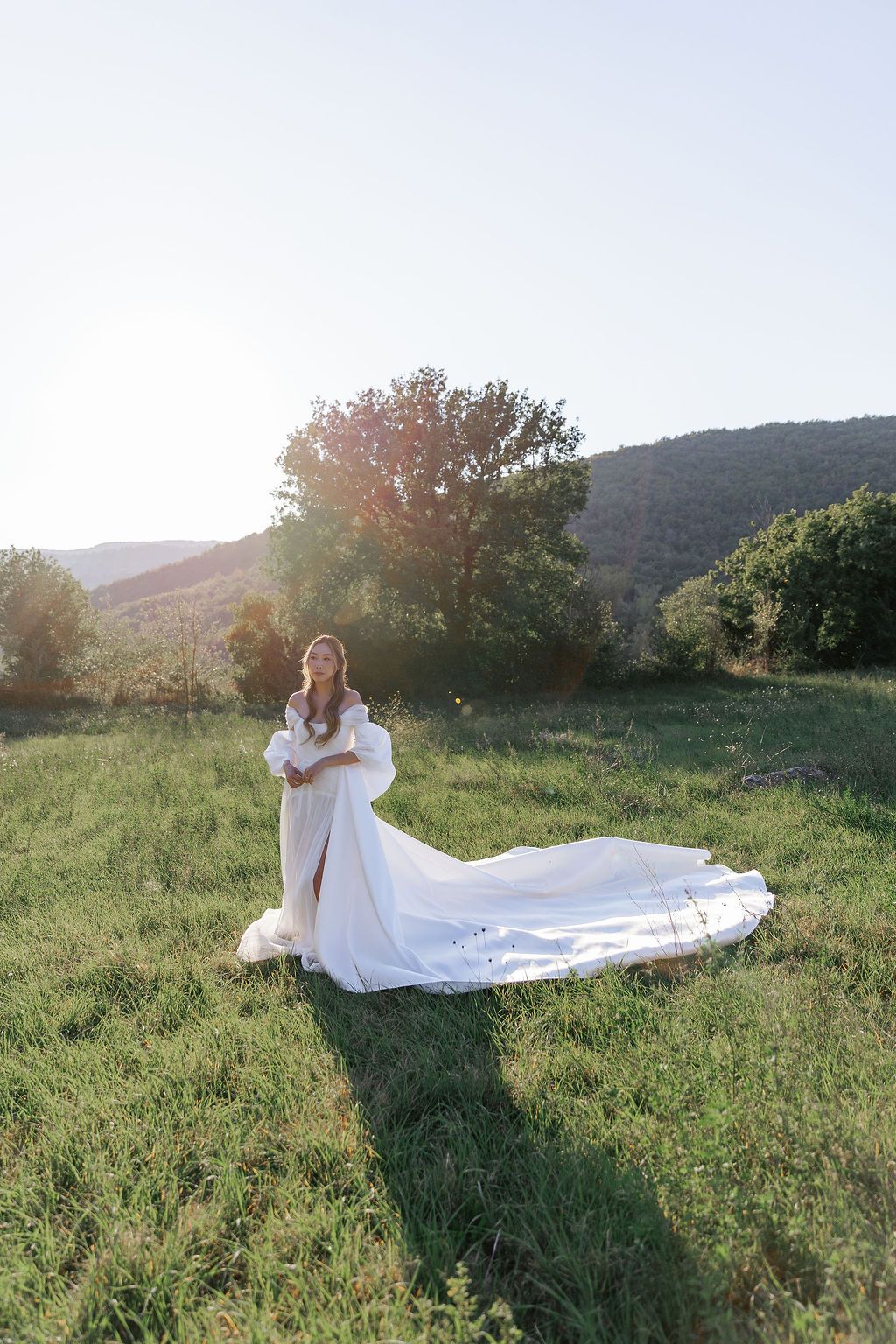 A flowing white wedding dress billows gracefully across a sunlit hillside meadow during golden hour in Tuscany, Italy.