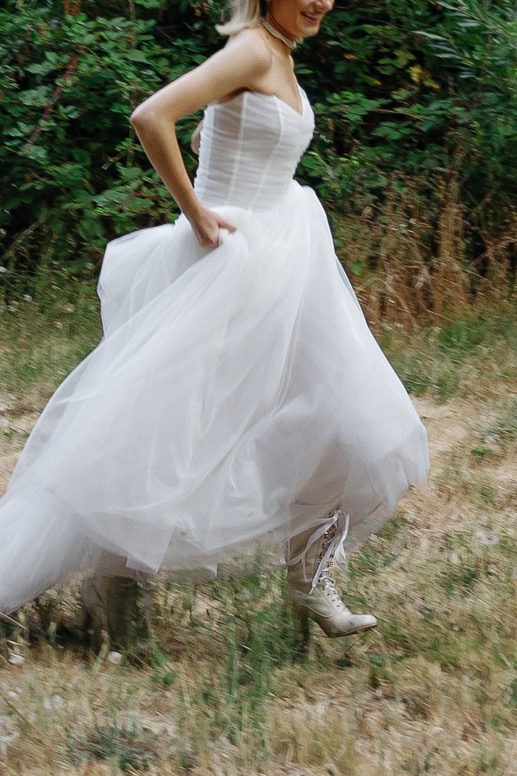 Close-up of white tulle wedding dress and sneakers in motion against grass.