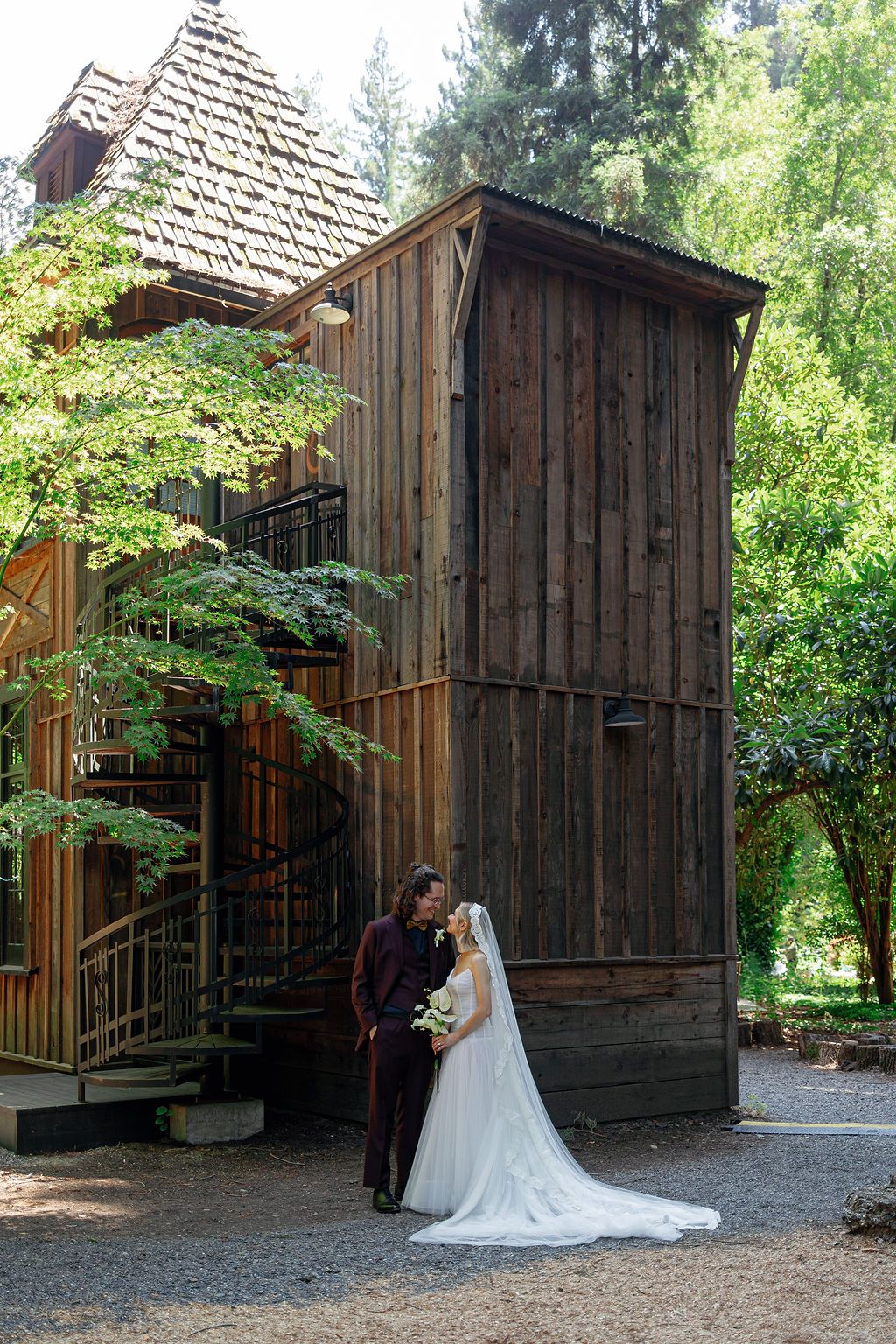 A rustic wooden chapel with a shingled roof stands in a lush forest setting during a wedding ceremony.