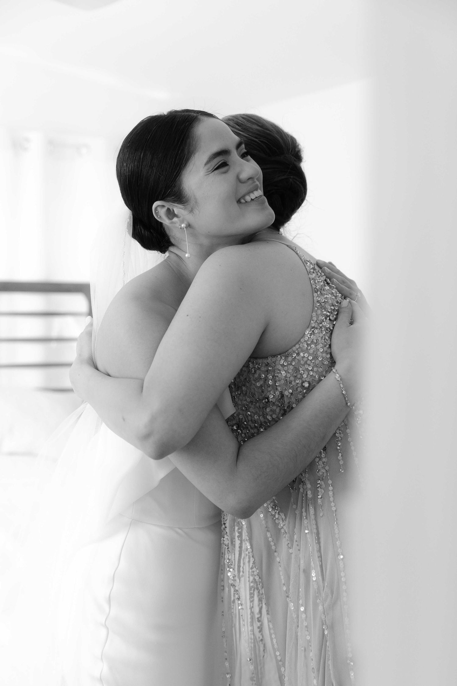 Two people share a warm embrace while wearing elegant sparkling formal dresses in this black and white photograph.