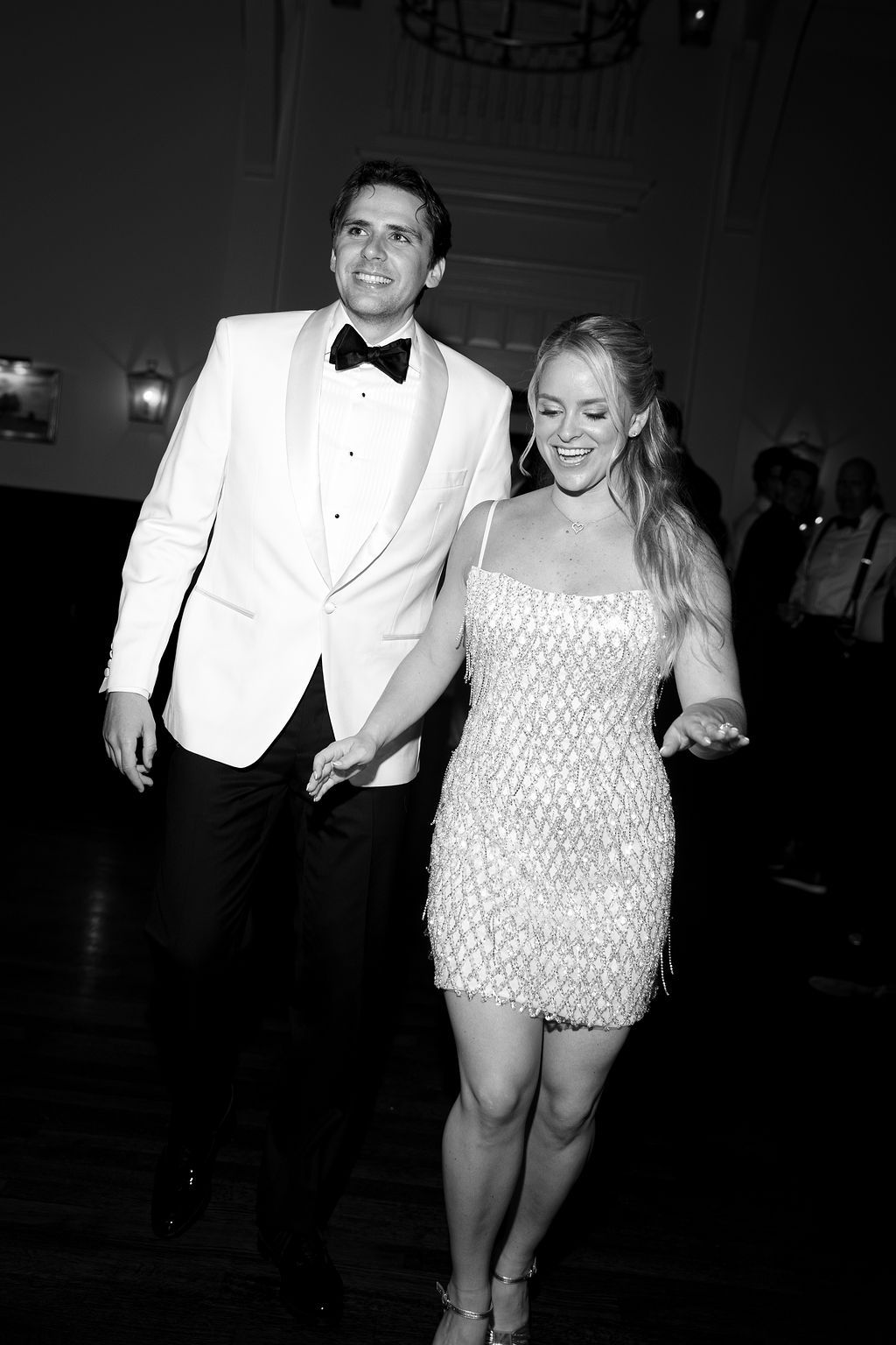 A couple in formal attire dancing together at an elegant event, with the person in white wearing a sparkly dress.