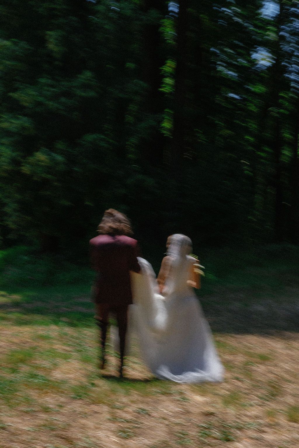 Motion-blurred figures moving through a dark wooded area creating an ethereal effect.