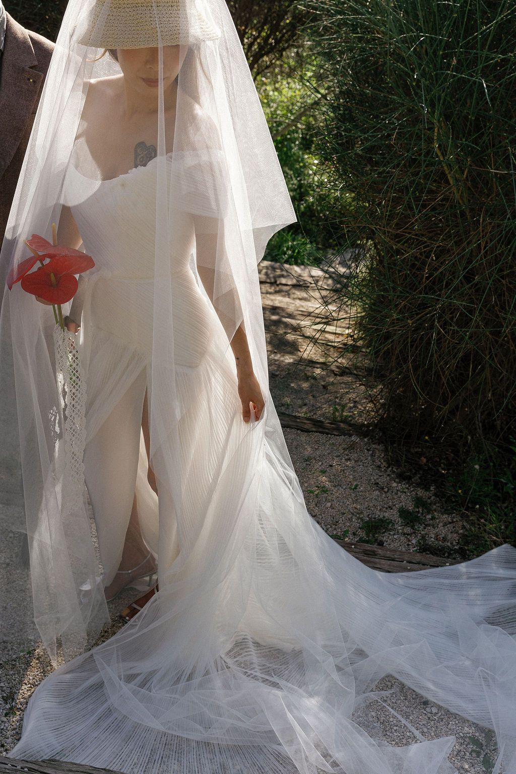 A flowing white wedding dress with a long train photographed in a series of outdoor shots with red floral accents in Tuscany, Italy.