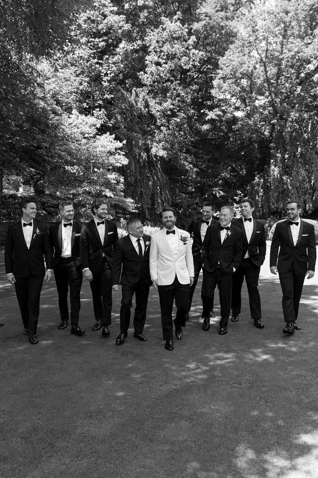 Wedding party in formal black and white attire walking together on a tree-lined path in elegant black and white style.