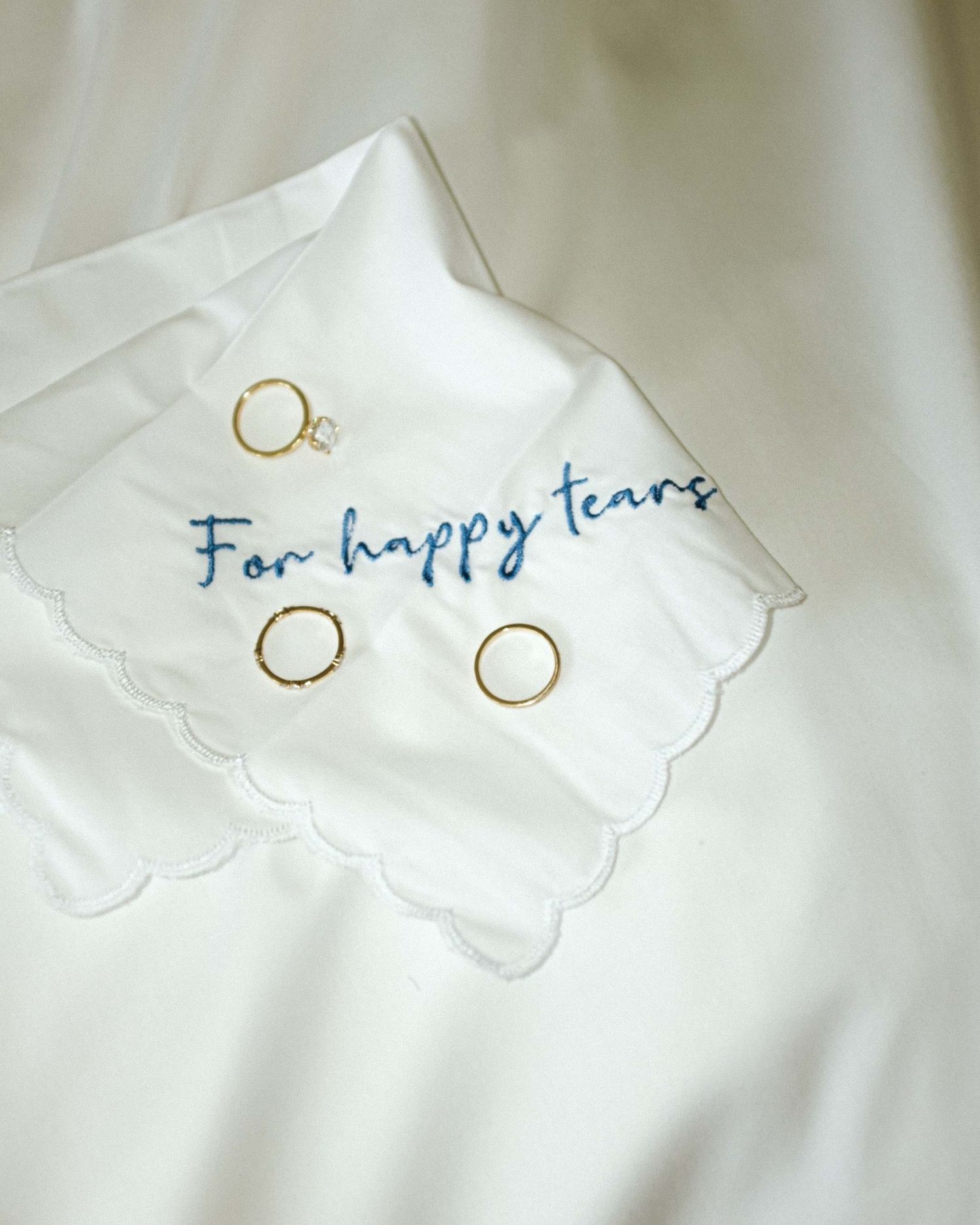 Handwritten text reading 'happy tears' with a small ink drawing in blue on a white cloth napkin or handkerchief.
