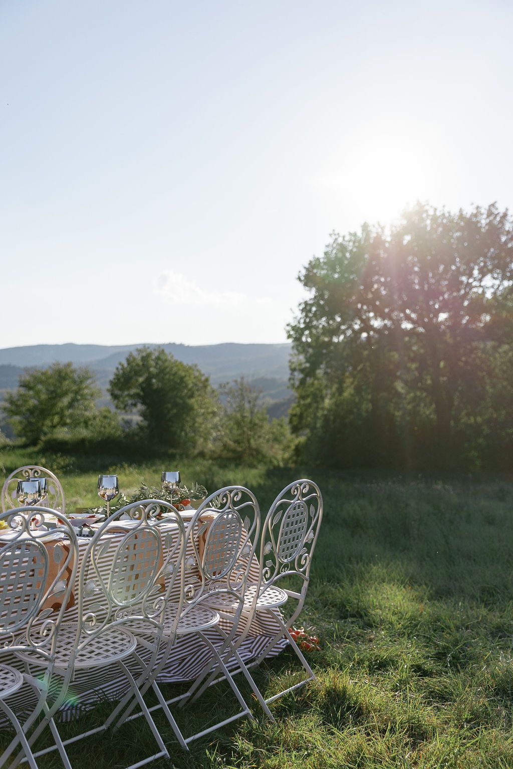 White ornate garden chairs arranged in rows on a grassy hillside at sunset in Tuscany, Italy.