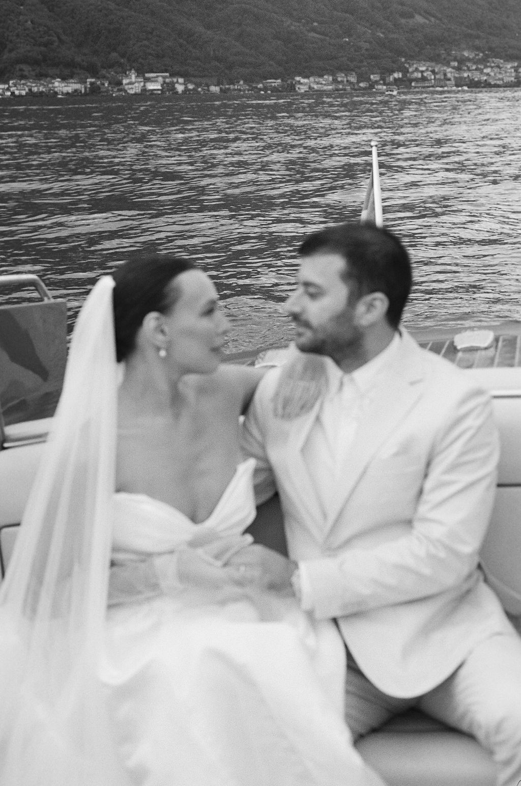 Black and white wedding photo of couple on a boat with coastal village in background in Lake Como.