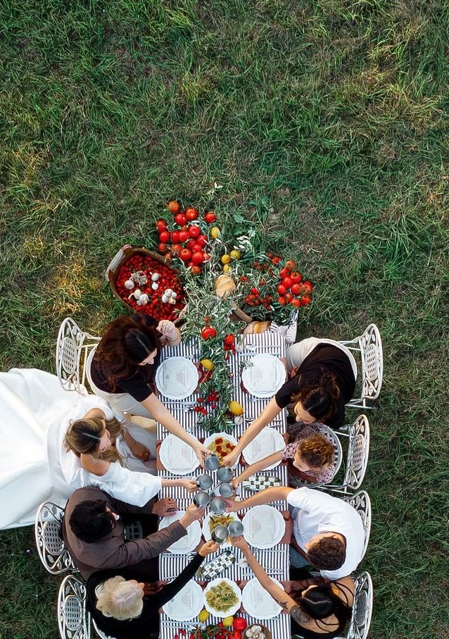 Overhead view of people having an elegant outdoor picnic with white and striped tablecloths and red floral arrangements.