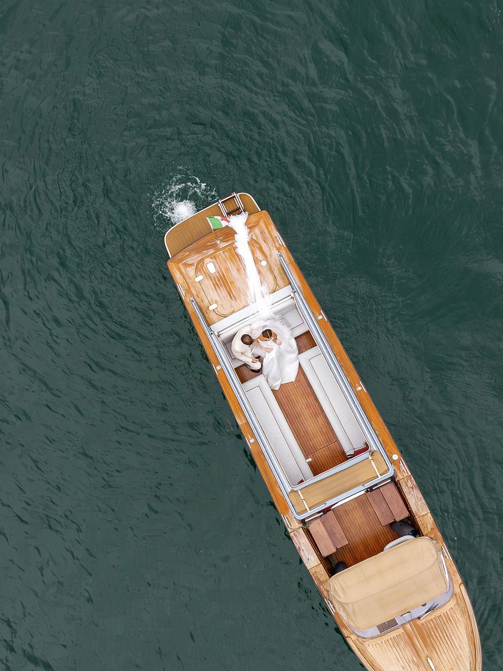 Aerial view of an Italian wooden boat with white trim floating on dark turquoise waters in Lake Como,  Italy.