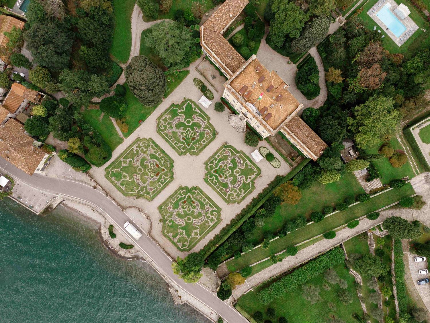 Aerial view of an ornate garden with geometric patterns next to a waterfront villa and lush green grounds in Lake Como, Italy.
