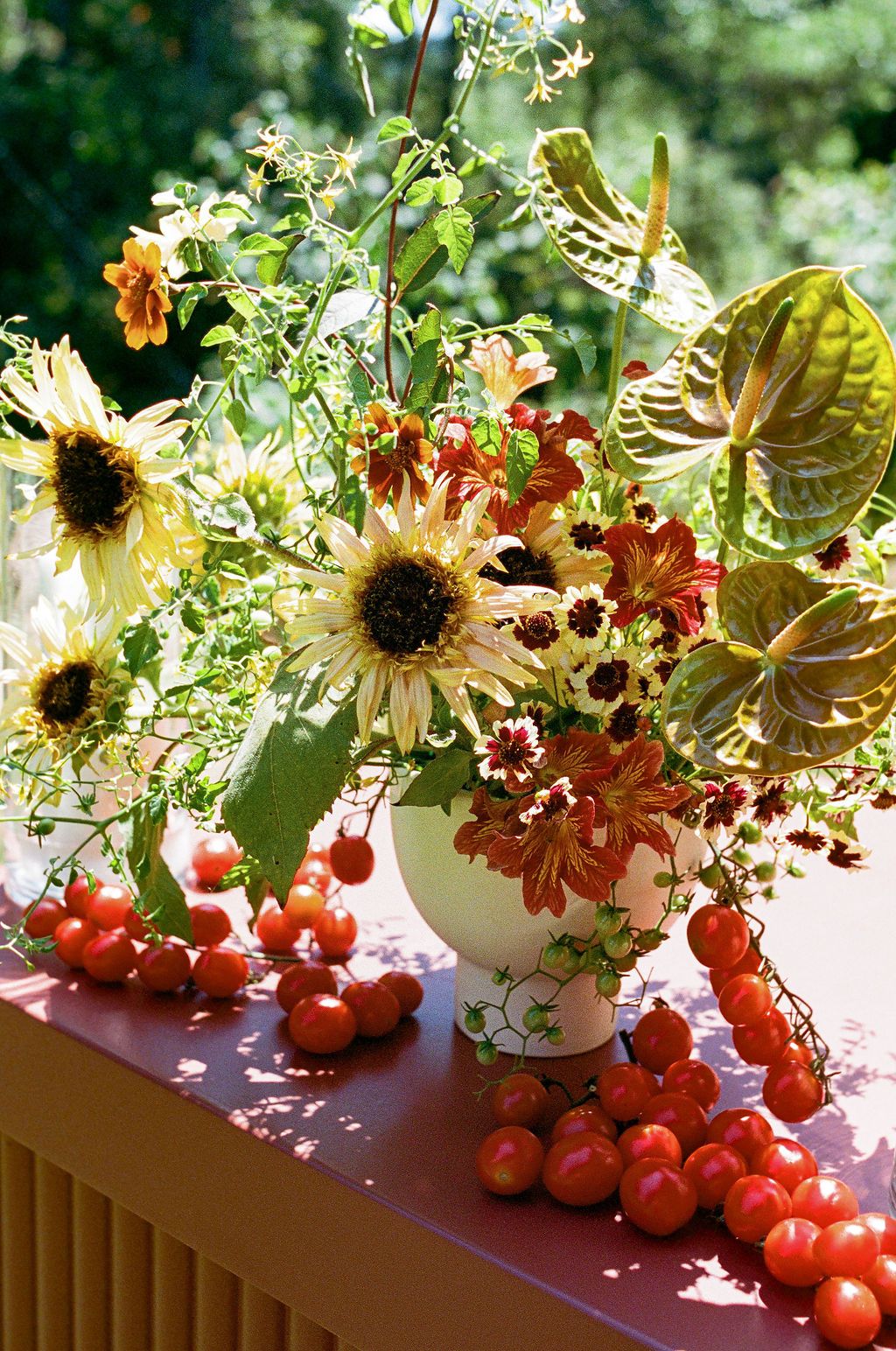 Floral centerpieces with sunflowers and white wildflowers in vases alongside fresh red tomatoes on a sunlit surface in California.
