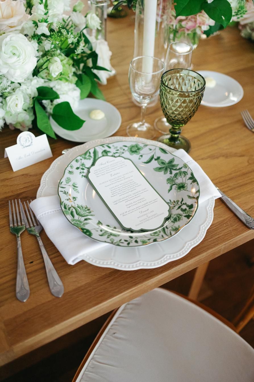 An elegant place setting with green floral china, white roses, and a vintage-style green goblet.