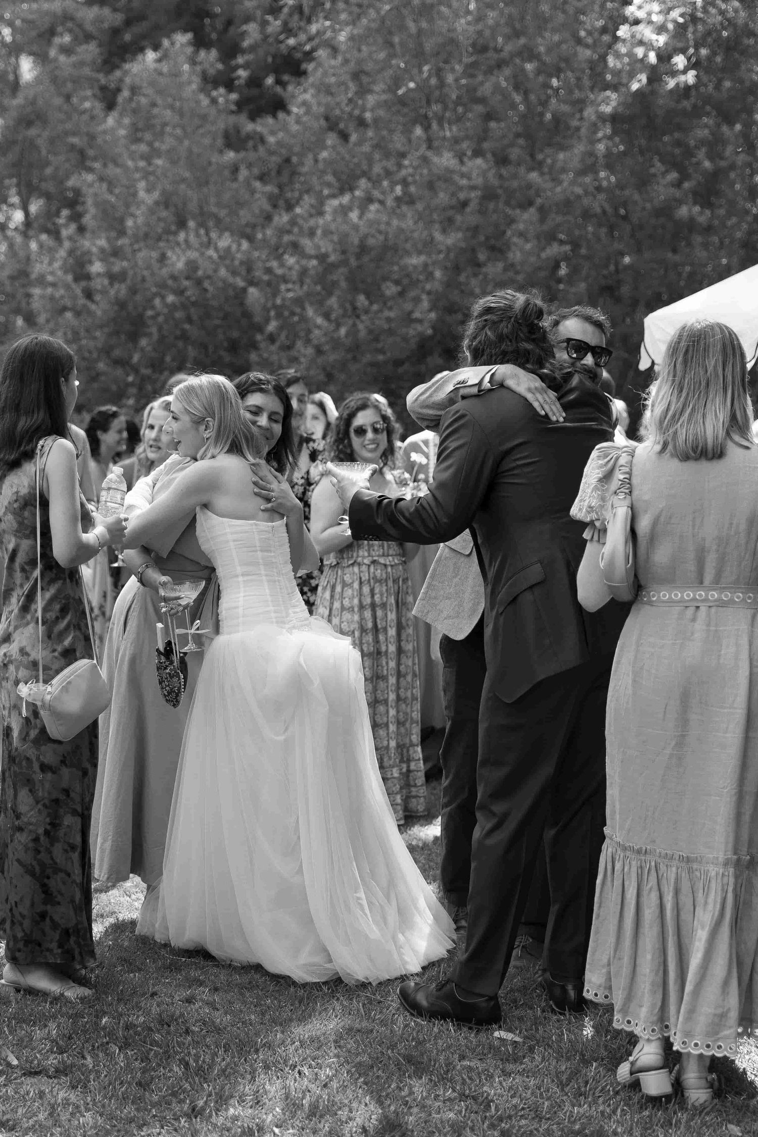 Black and white photo of bride and groom embracing at outdoor wedding reception surrounded by guests.