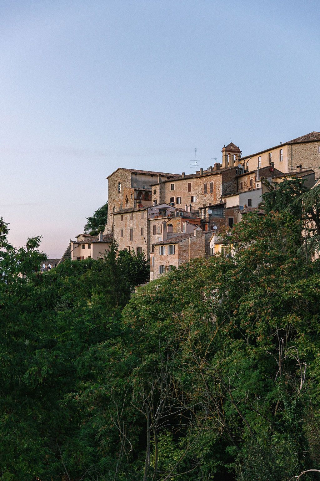 Ancient stone buildings perched on a hillside overlooking lush green forest in an Italian medieval village in Tuscany, Italy.