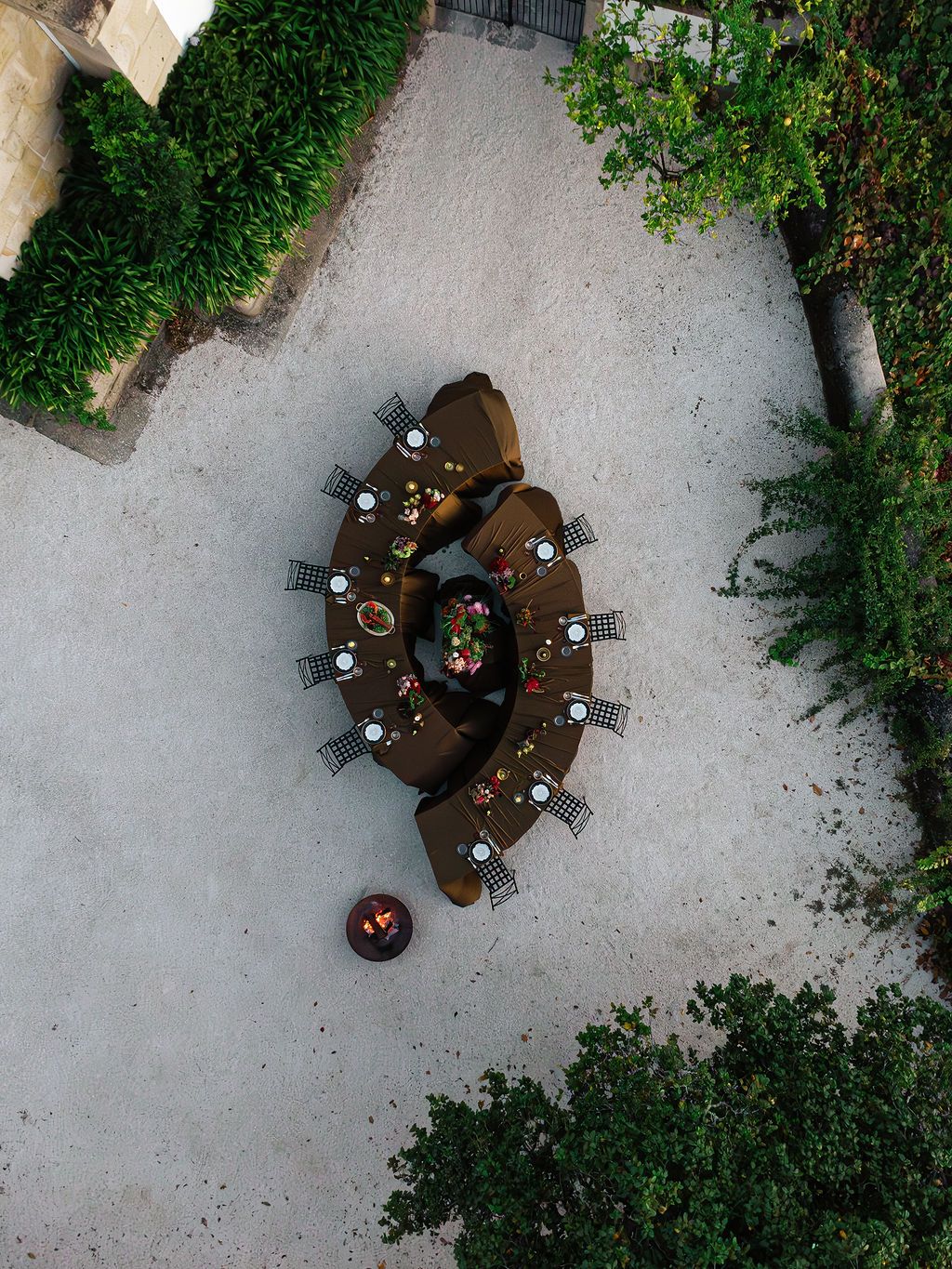 Aerial view of a round wooden table with chairs surrounded by lush greenery in an outdoor garden setting.