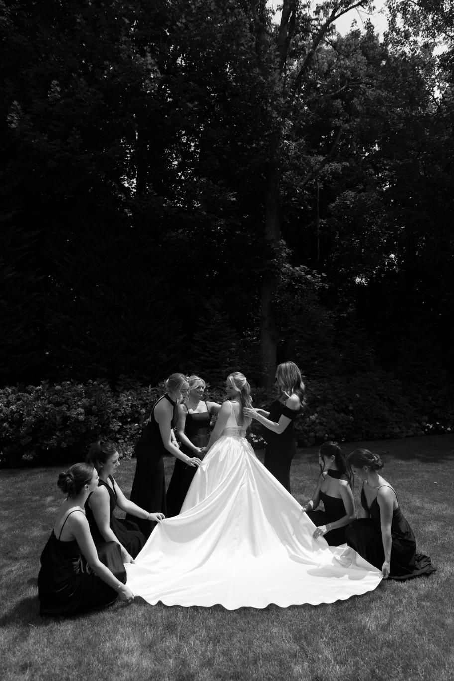 A sequence showing people laying in a circle on grass, spreading out a flowing white dress in an artistic arrangement.