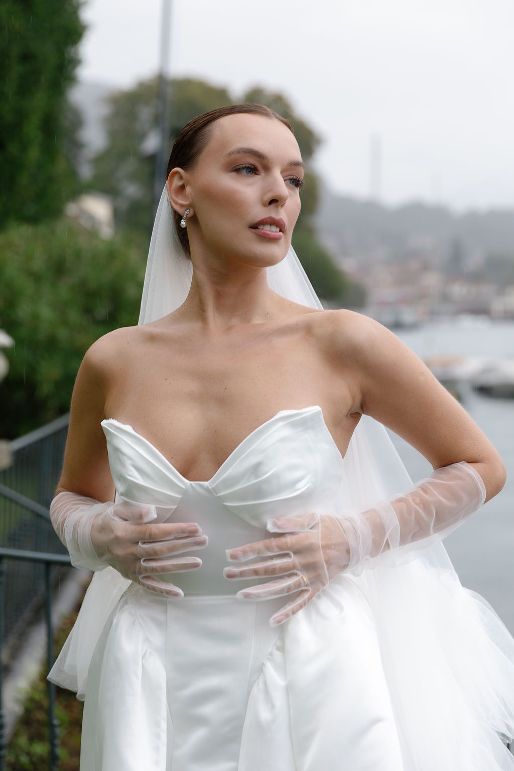 Elegant white wedding dress with sweetheart neckline and sheer long gloves against coastal backdrop in Lake Como.