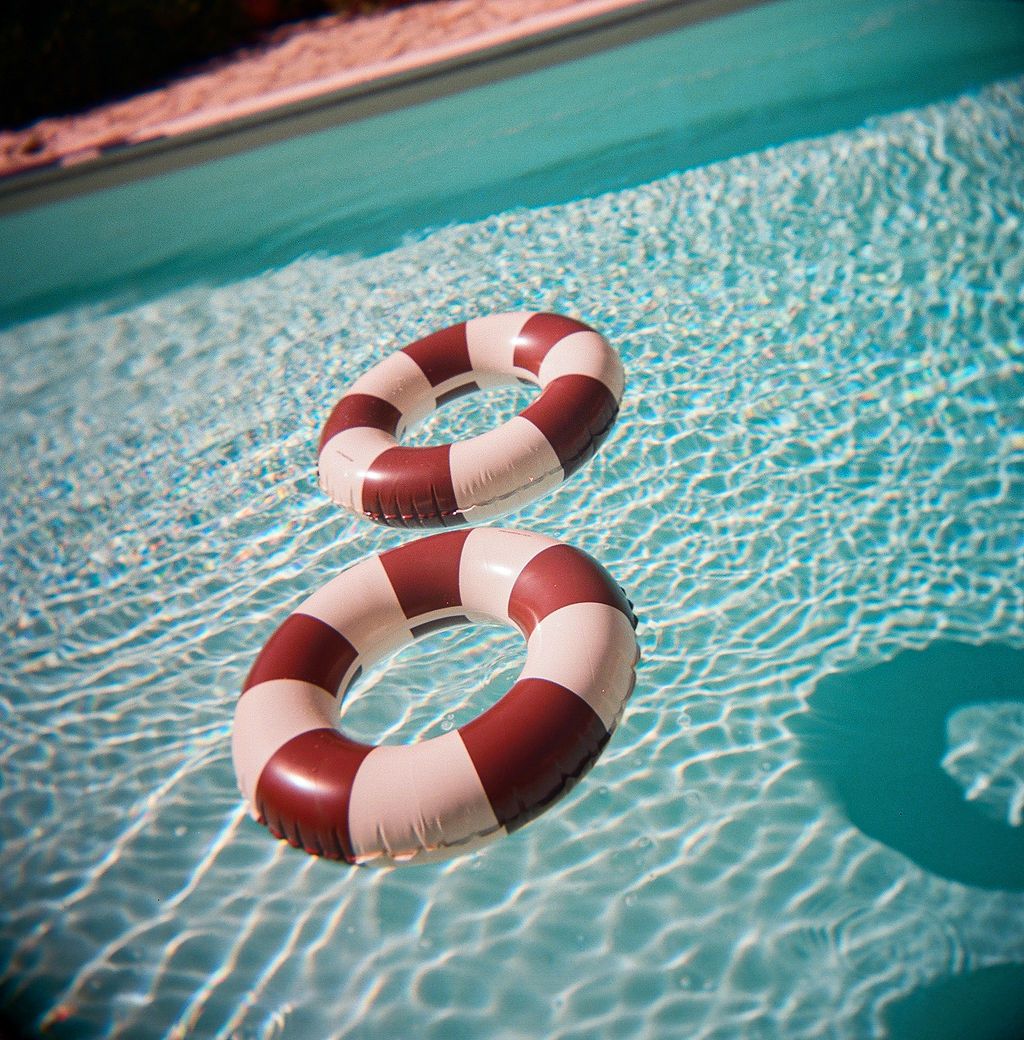 A red and white life preserver ring floating in bright turquoise pool water with rippling reflections in Tuscany, Italy.