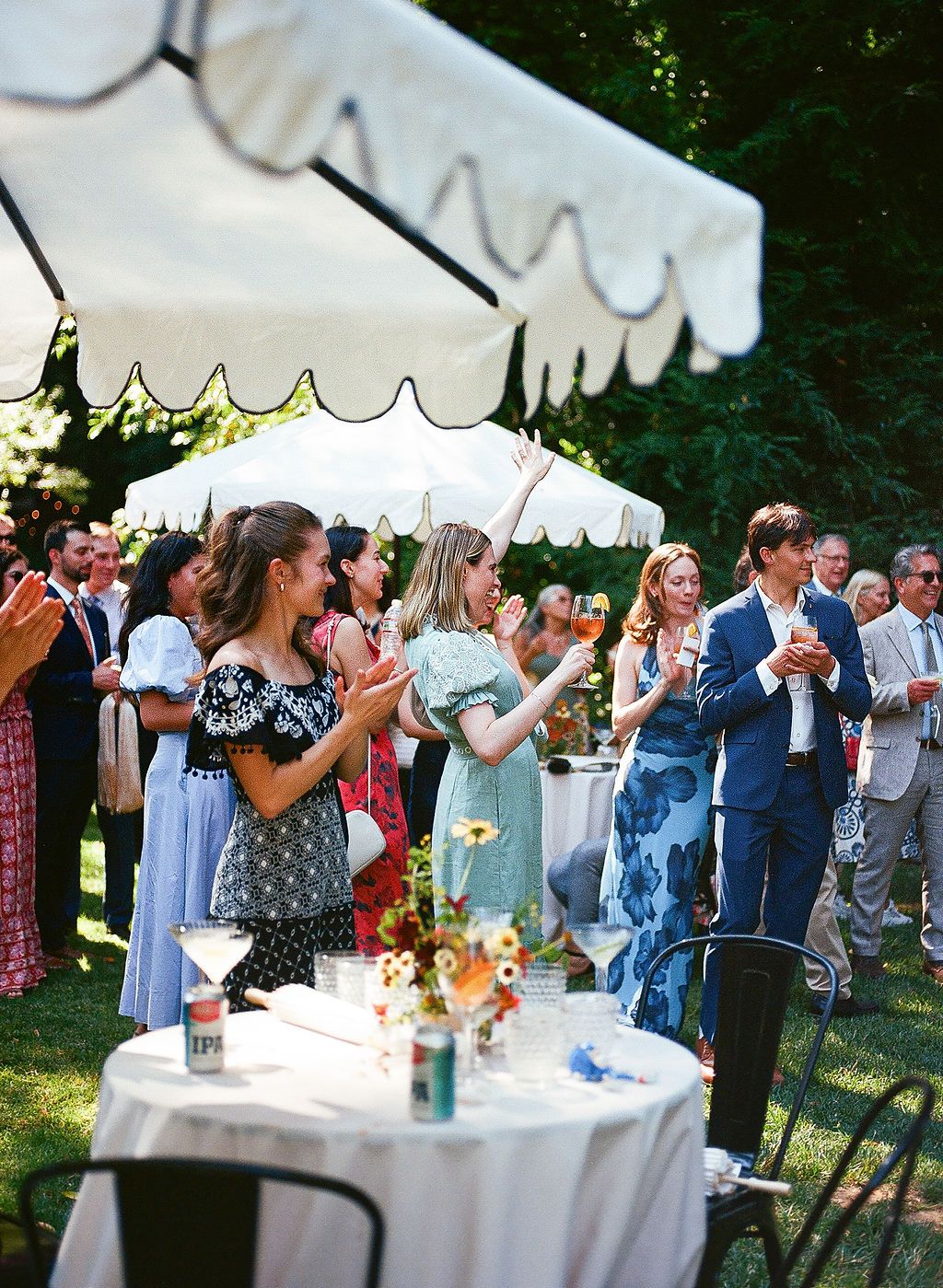 Wedding reception under a white tent with guests mingling around decorated tables.