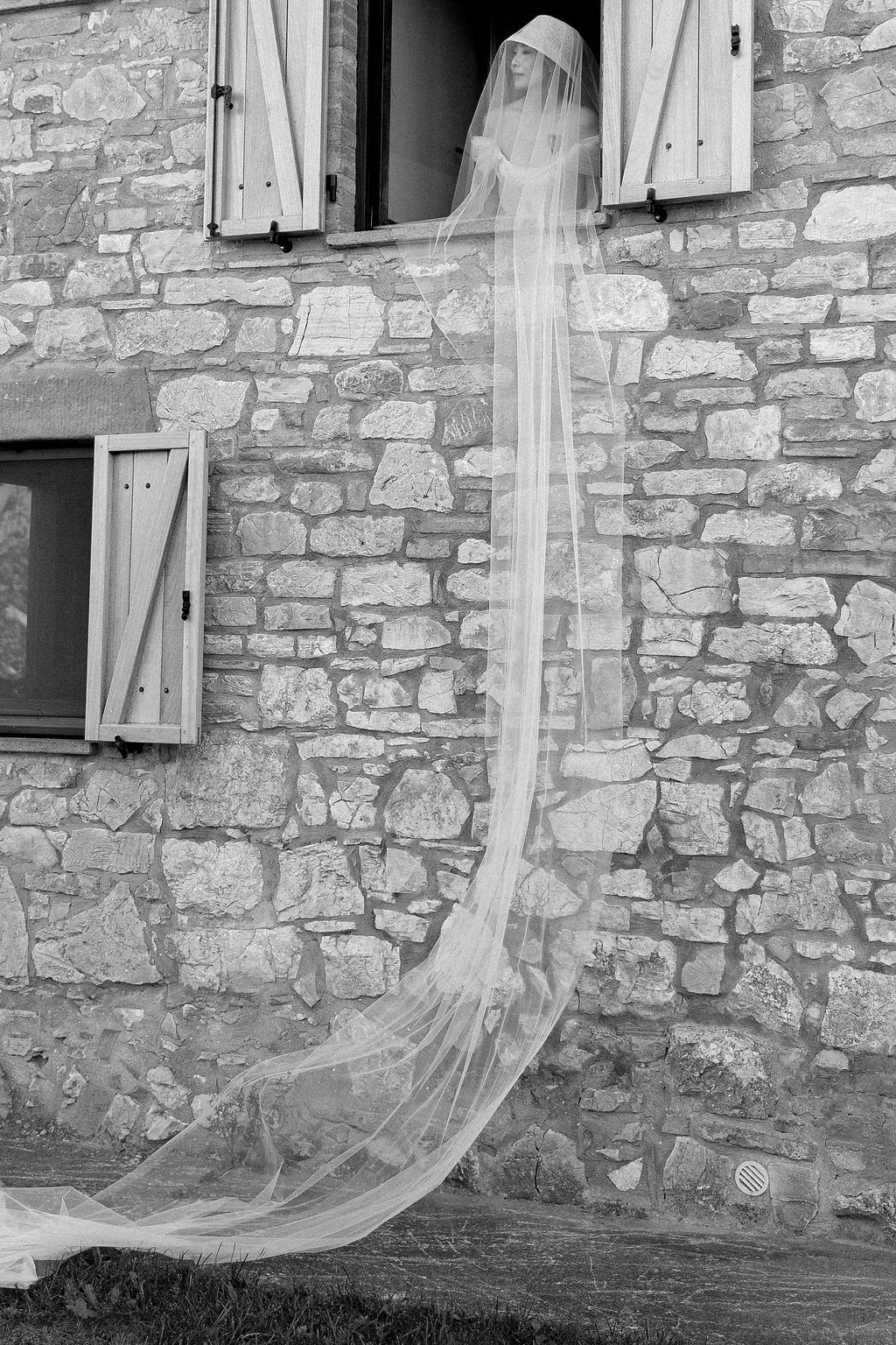 Sheer white curtains billow through windows of a rustic stone building creating an ethereal atmosphere in Tuscany, Italy.
