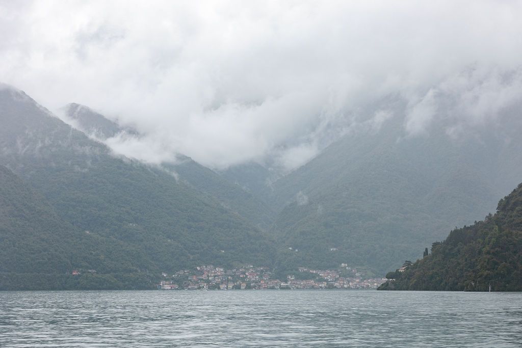 Panoramic view of a misty mountain lake surrounded by snow-capped peaks and cloudy skies in Lake Como.