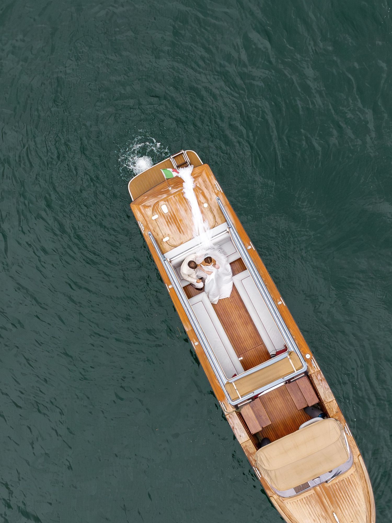 Aerial top-down view of a luxury wooden yacht sailing on calm green ocean waters.