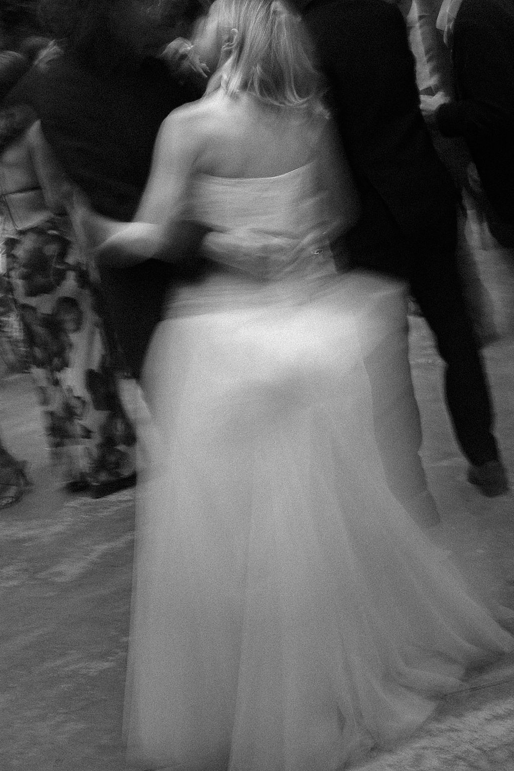 Blurred motion shot of white wedding dress twirling on dance floor.