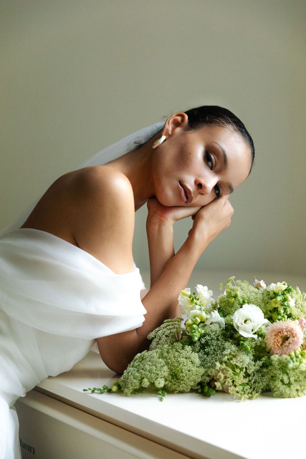 Elegant portrait with white flowers and greenery on table against neutral background, showcasing soft draping fabric.