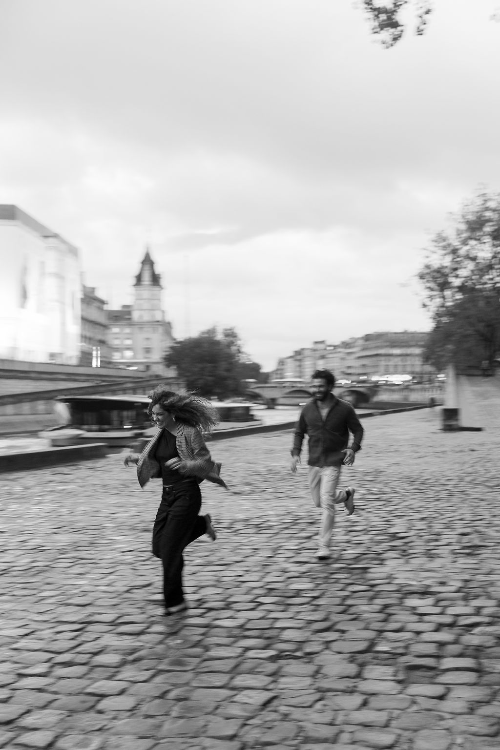 A sequence of people running across a cobblestone street in black and white, creating a dynamic motion effect in Paris, France.