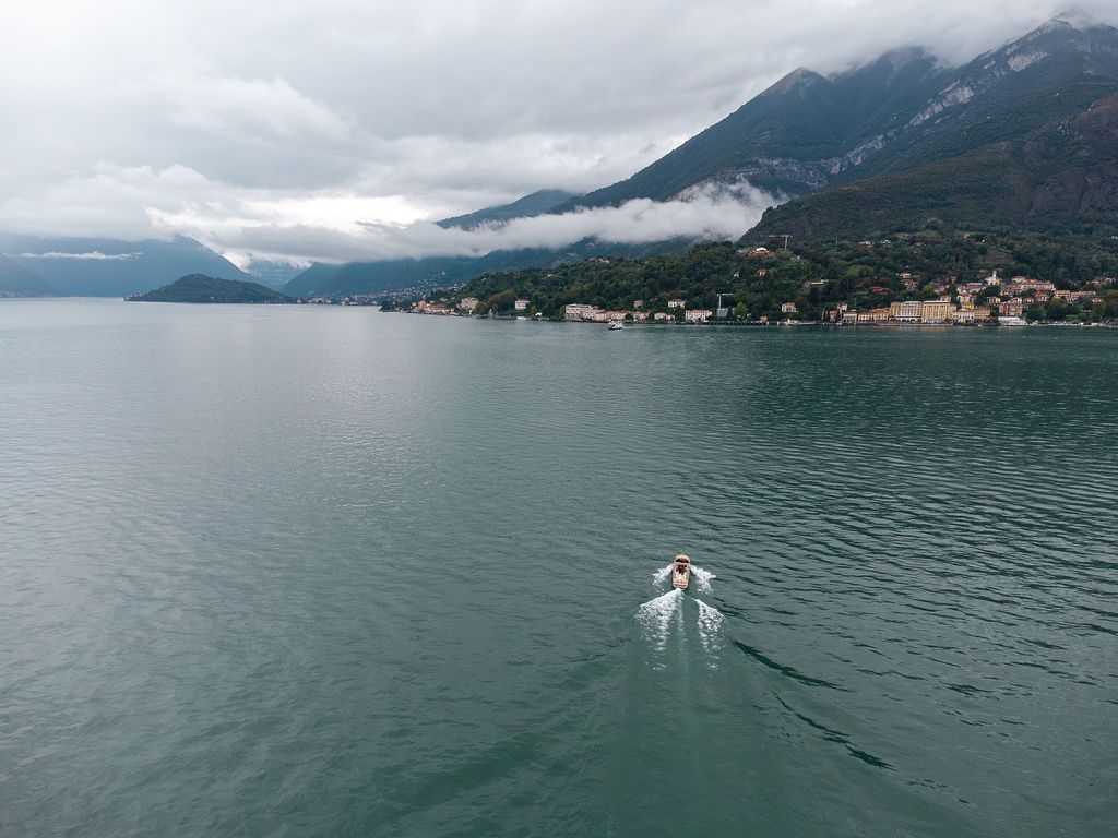 Aerial shot of boat leaving wake trail on misty Lake Como surrounded by mountains.