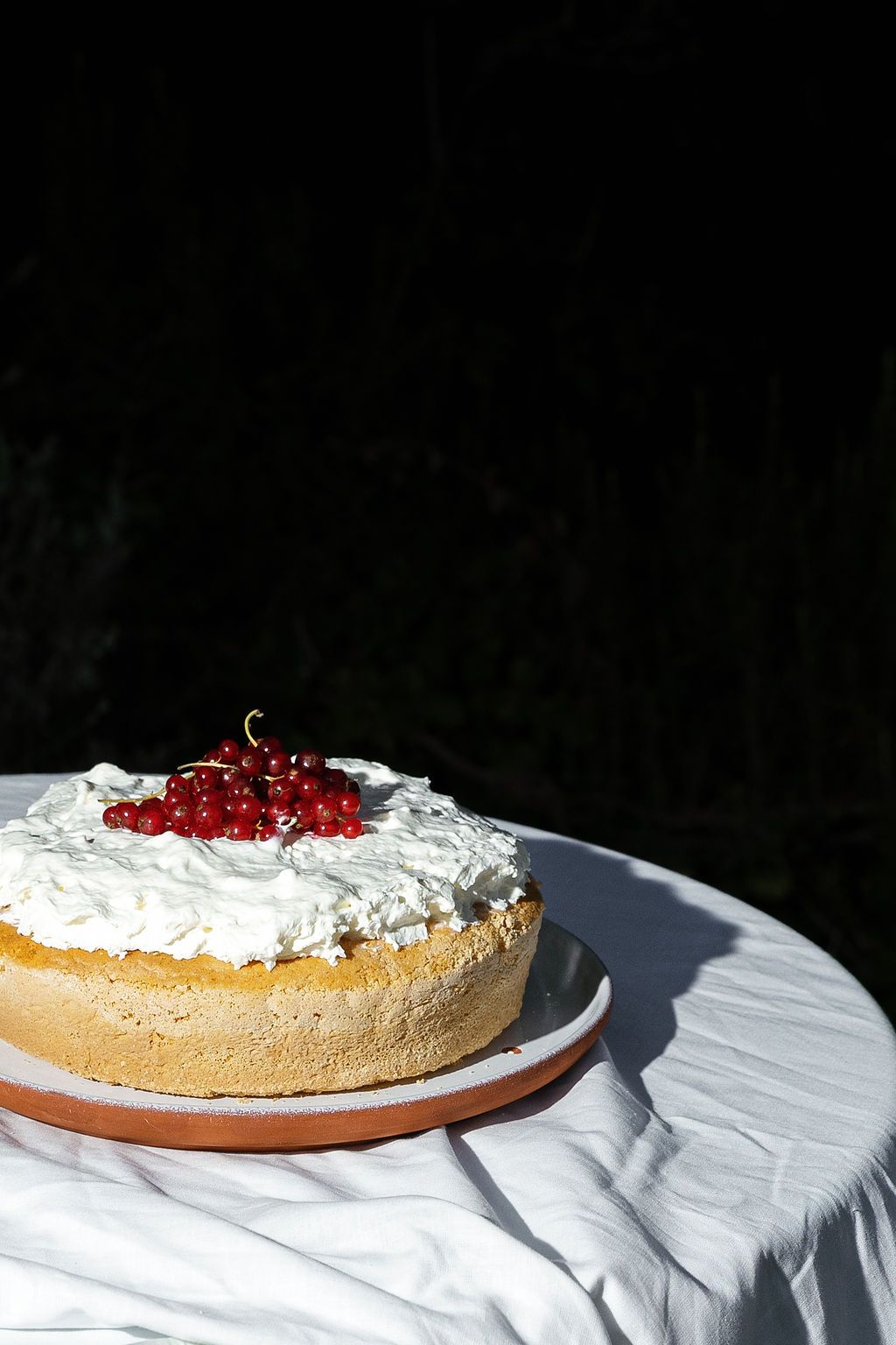 A cream-colored pie topped with whipped cream and red cherries on a white tablecloth in Tuscany, Italy.
