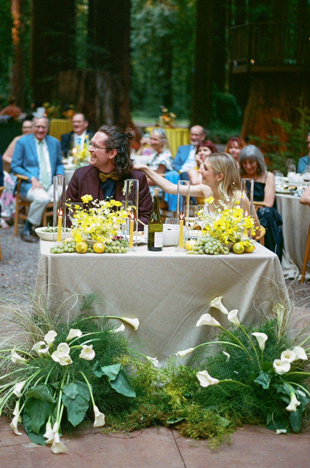 Long dining table decorated with white calla lilies and greenery for an outdoor wedding reception.
