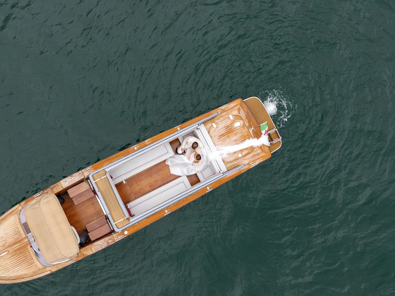 Aerial top-down view of a wooden luxury yacht sailing on calm green ocean waters.