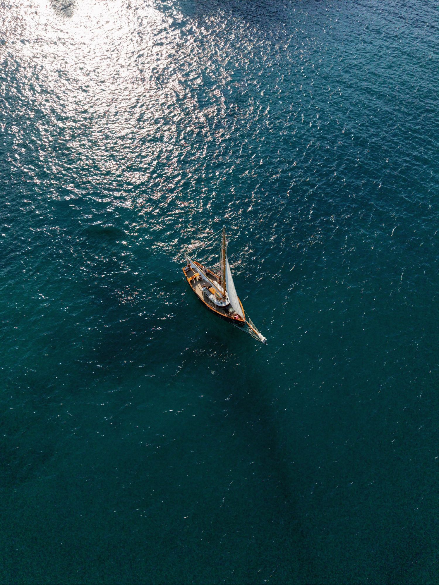 Aerial drone view of a classic wooden sailboat sailing on turquoise blue ocean waters on a sunny day.